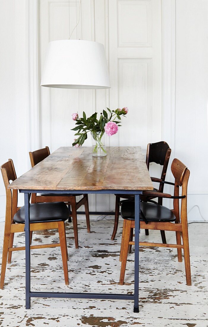 Rustic table and 60s-style chairs below contemporary pendant lamp with white lampshade in dining room with distressed wooden floor