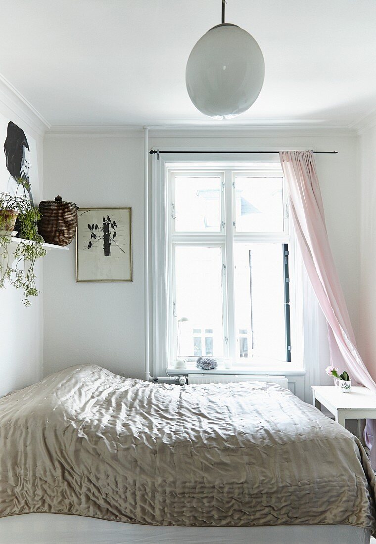 Doppelbett mit glänzender Tagesdecke vor Fenster in weißem Schlafzimmer