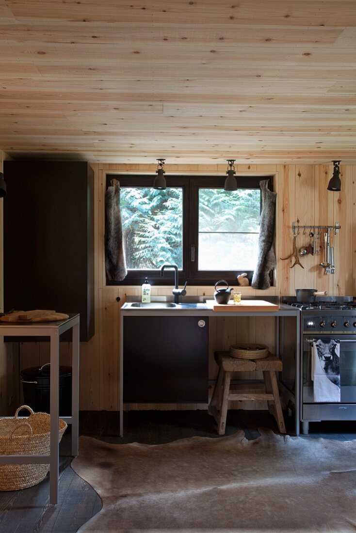 Minimalist kitchen counter below window in wood-clad kitchen with animal-skin rug