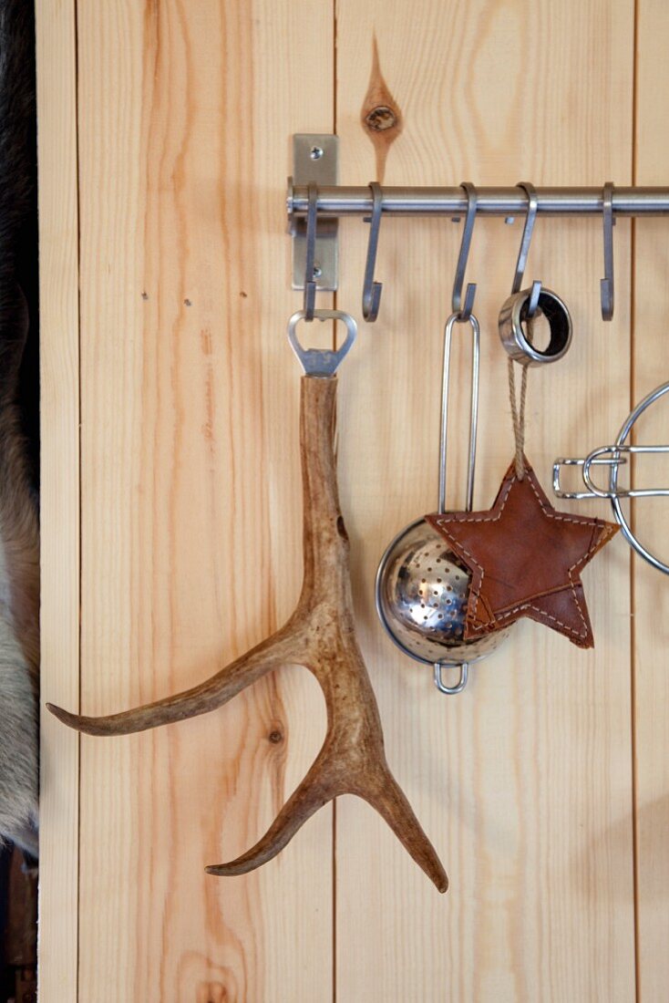 Bottle opener with antler handle and kitchen utensils hanging from hooks on stainless steel rail