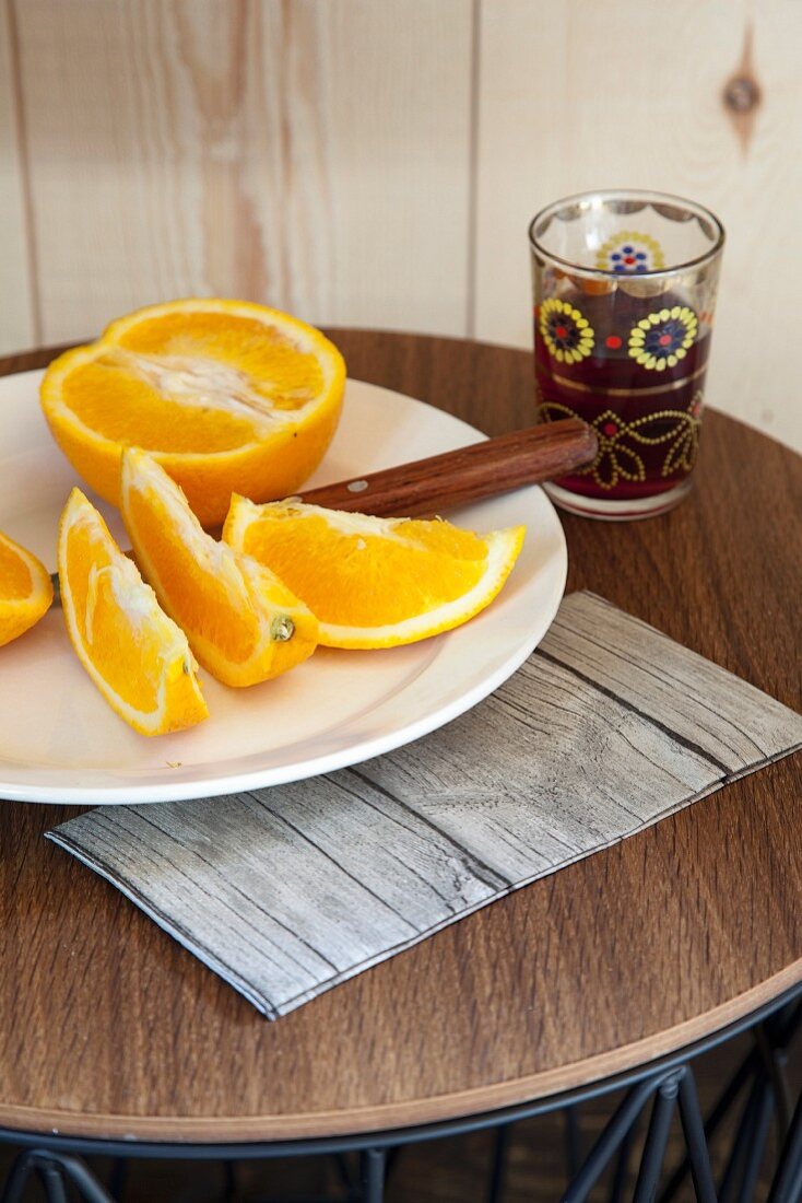 Orangenschnitzen auf weißem Telle und Teeglas auf rundem Beistelltisch