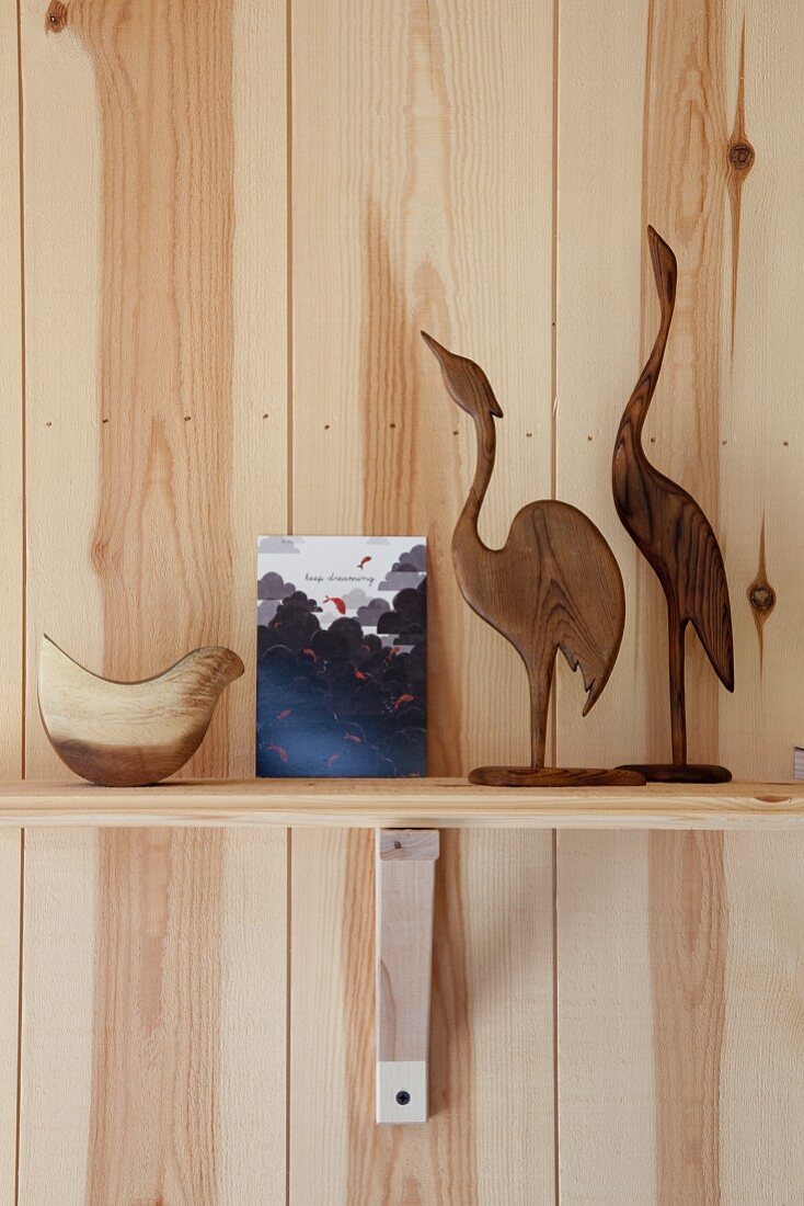 Vogelfiguren aus Holz auf Konsolenregalbrett vor Kiefernholzwand arrangiert