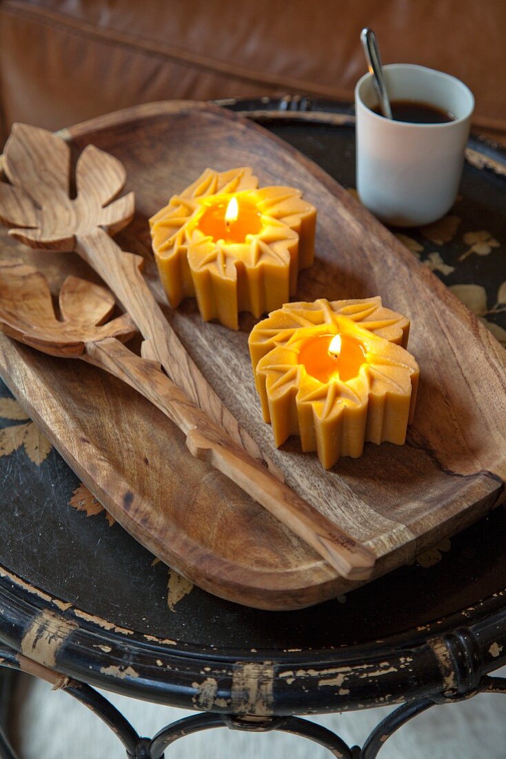 Honey-coloured tealights on wooden dish next to salad servers