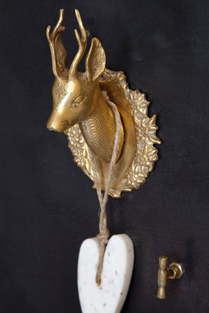 Heart-shaped car of soap hanging from miniature, brass stag's head as tap fitting on black wall