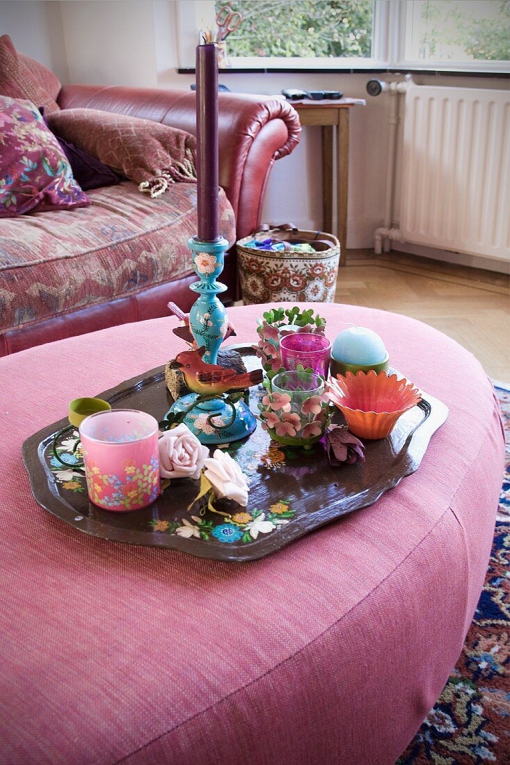 Collection of tealight holders and candle lanterns on tray on pink ottoman
