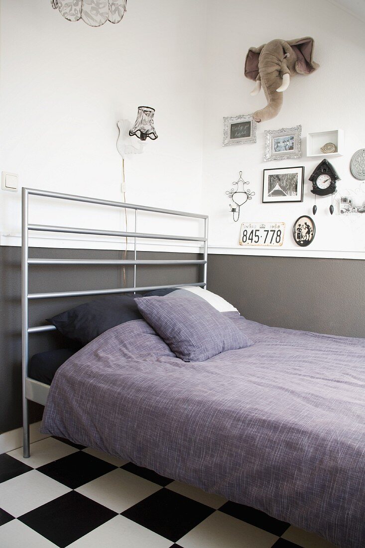 Bett mit modernem Metallgitter Kopfteil und lila Bettwäsche; an Wand Bilder und Stofftier-Trophäe