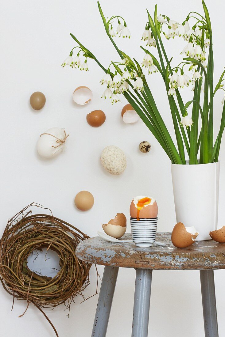 Märzenbecher und Eier auf altem Holzhocker; österliche Wanddeko mit Weidennest und verschiedenen, naturfarbenen Eiern