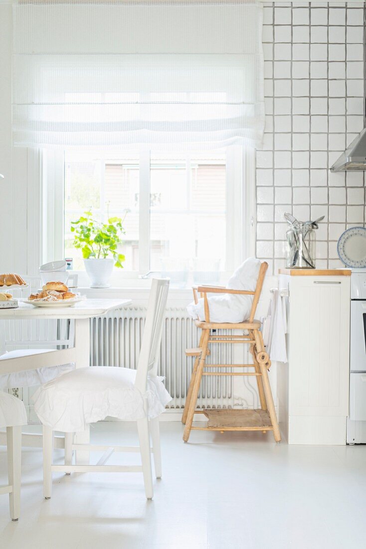 Essplatz mit gerüschten Sitzkissen und Kinderhochstuhl vor dem Fenster in weisser skandinavischer Küche