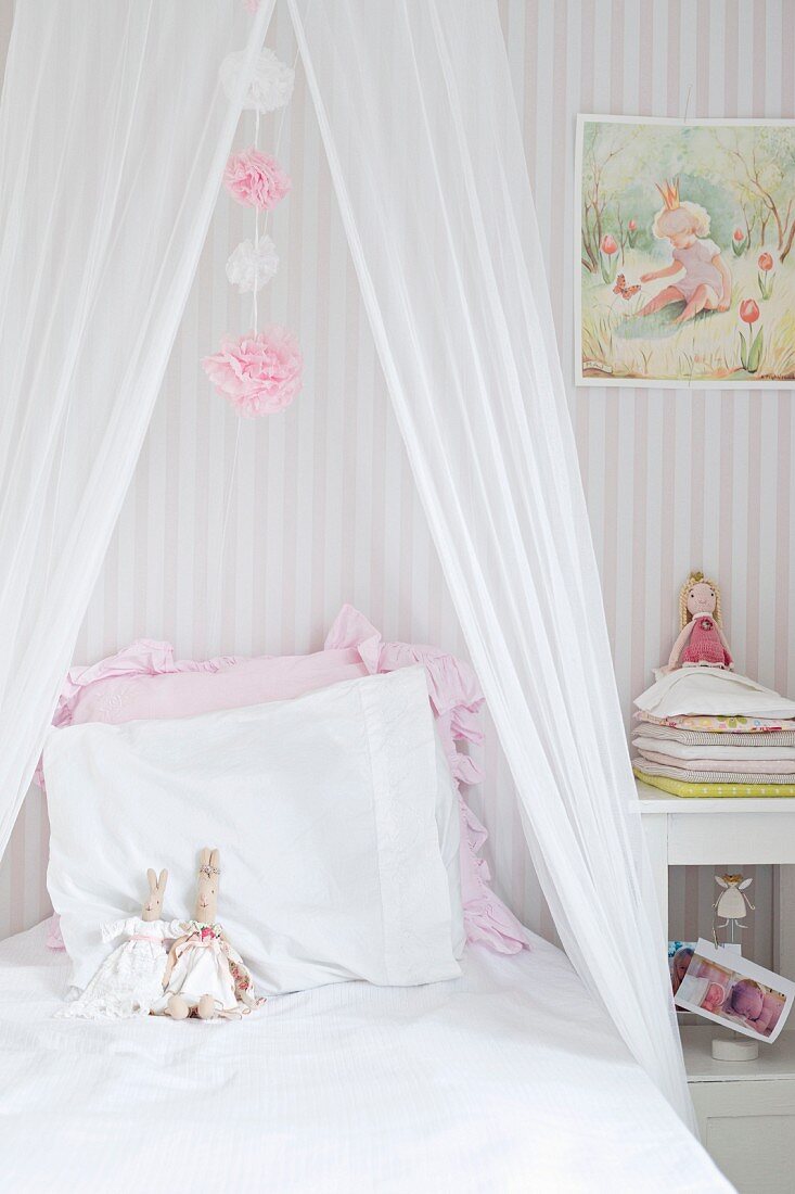Bett mit drapiertem Moskitonetz und Stoffhasen auf den Kopfkissen in romantischem Kinderzimmer
