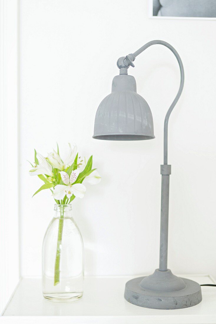 Grey-painted, vintage lamp and white irises in milk bottle on side table