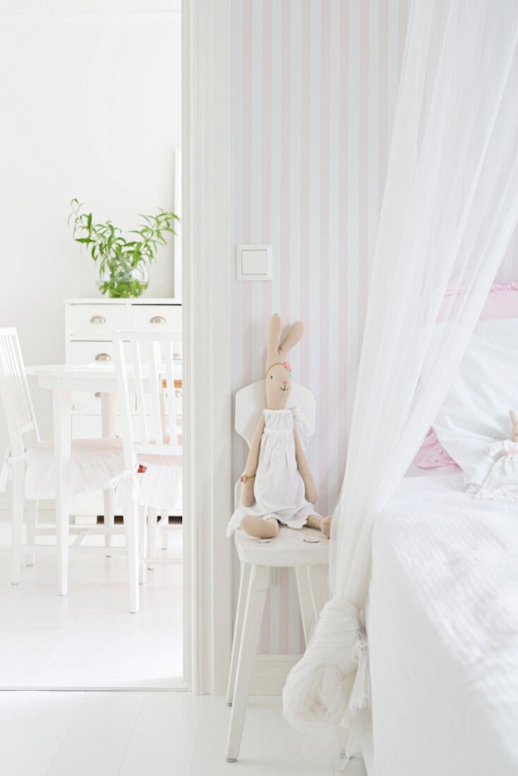 Stoffhase auf Holzstuhl neben einem Kinderbett mit Moskitohimmel; Blick in angrenzendes Esszimmer