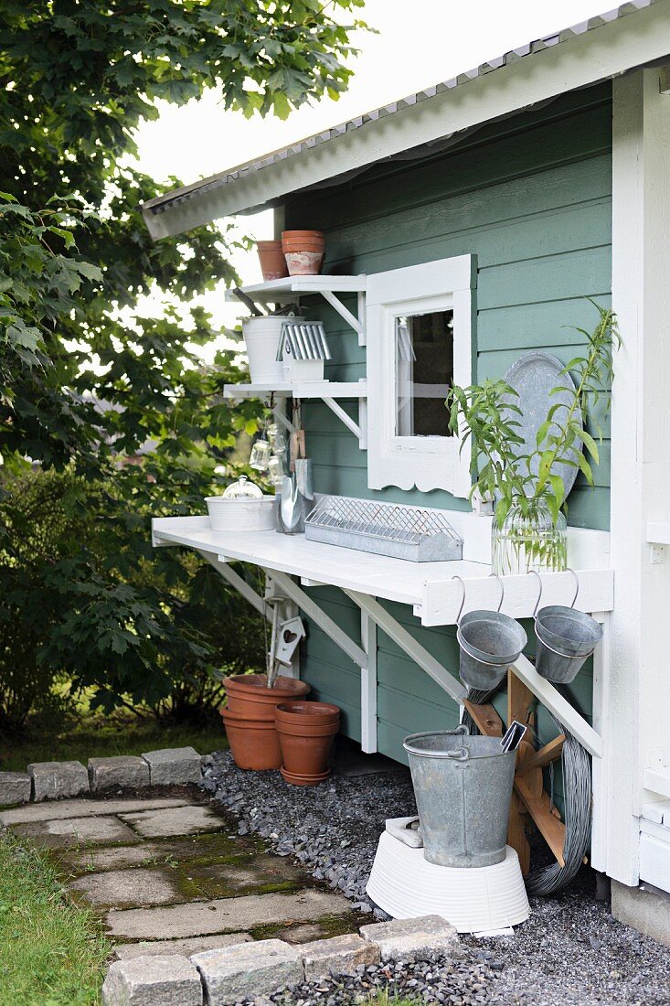 Gartenutensilien auf der Traufseite eines schwedischen Gartenhauses mit Tisch und Regalborden