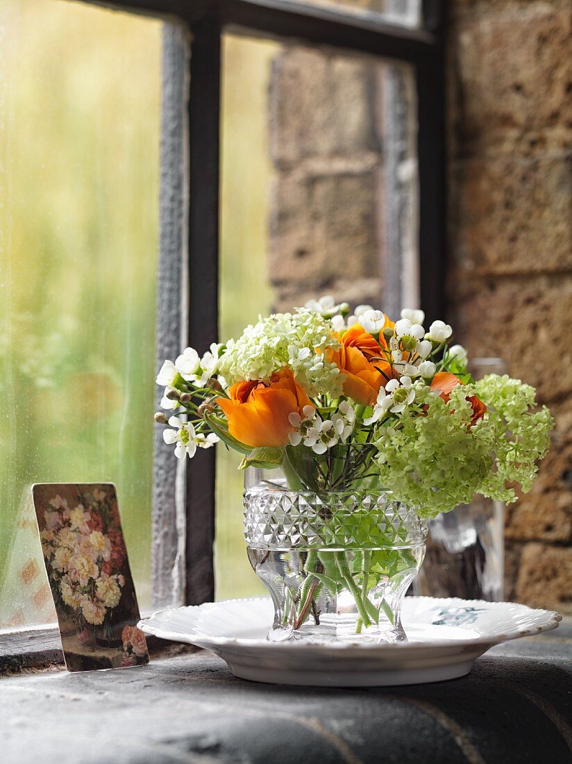 Kleiner Blumenstrauß mit Ranunkel und Schneeball in Glasvase am Fenster