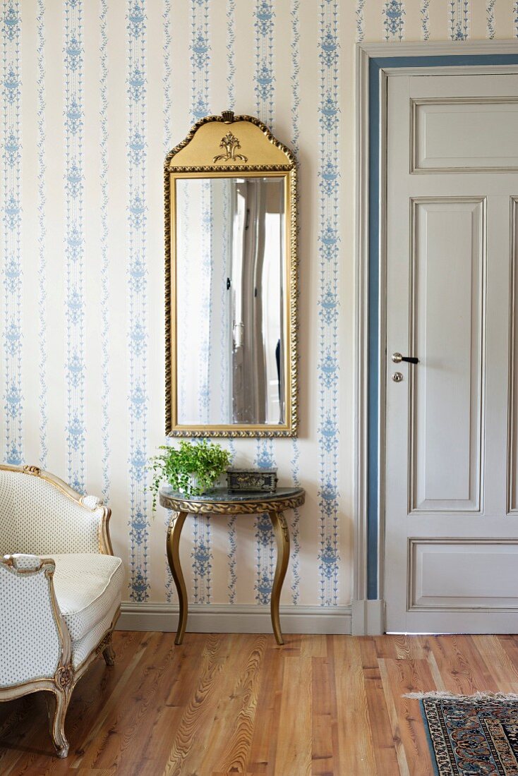 Framed mirror above console table with curved legs against wall with white and blue wallpaper