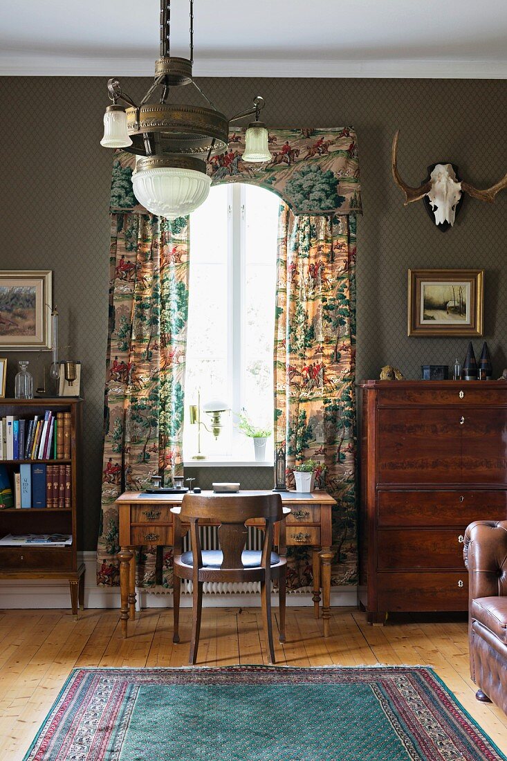 Ländliches Arbeitszimmer mit antikem Schreibtisch vor Fenster mit Schabracke und bodenlangem Vorhang