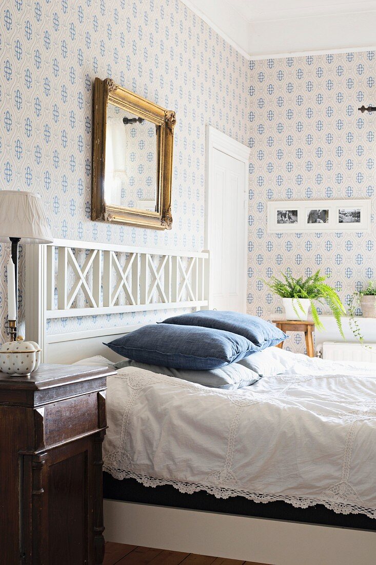 Double bed with white wooden headboard in rustic bedroom with white and blue patterned wallpaper