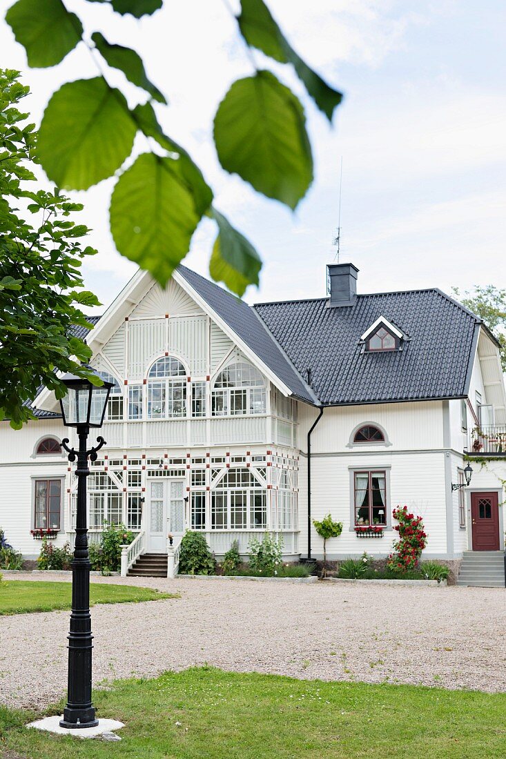Blick vom Garten mit traditioneller Standlaterne auf elegantes Landhaus in Weiß mit Wintergartenanbau
