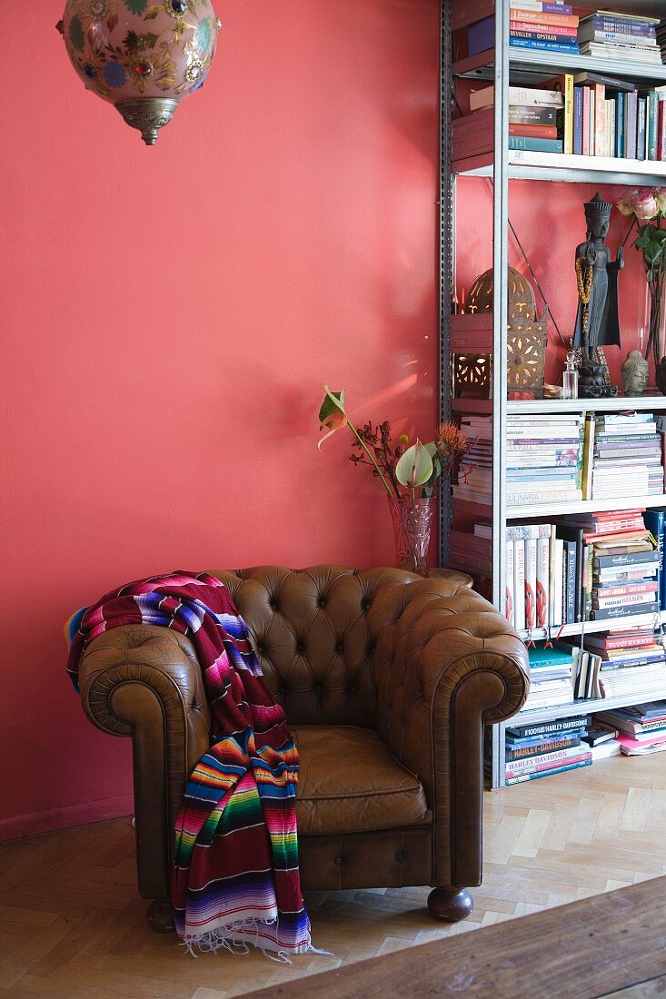 Eklektisches Flair mit traditionellem Ledersessel und Folkloreplaid vor Metall-Bücherregal an rosafarbener Wand