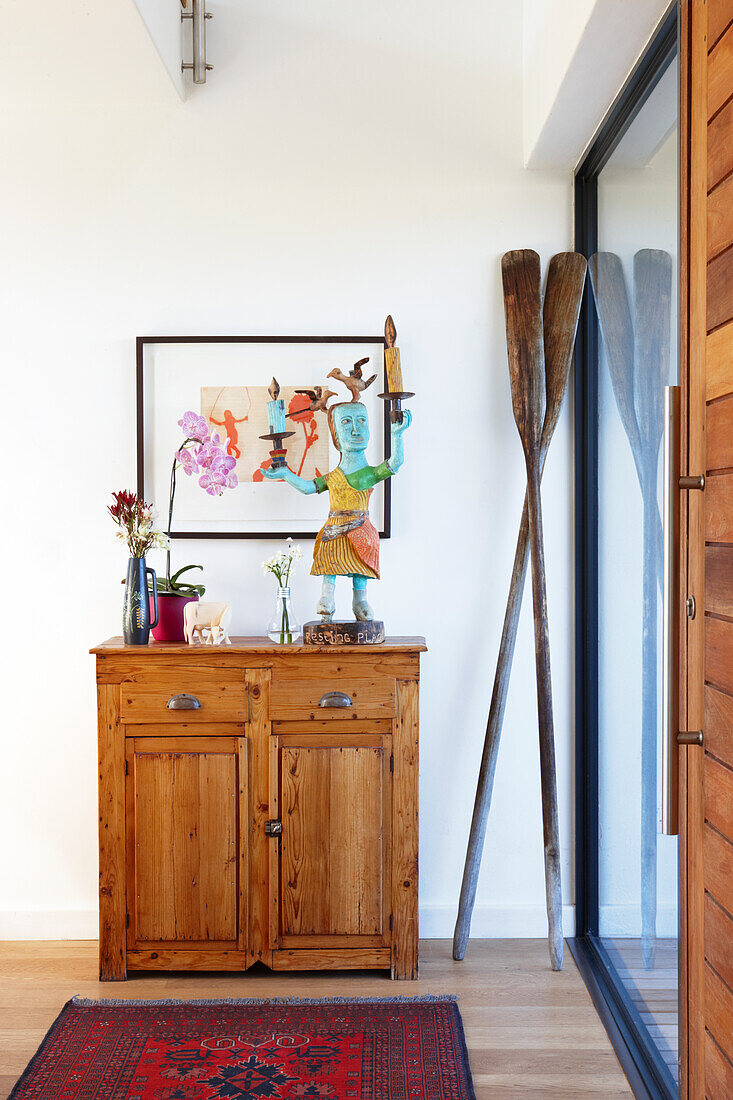 Painted wooden figurine on rustic wooden cabinet and wooden oars leaning against wall in foyer