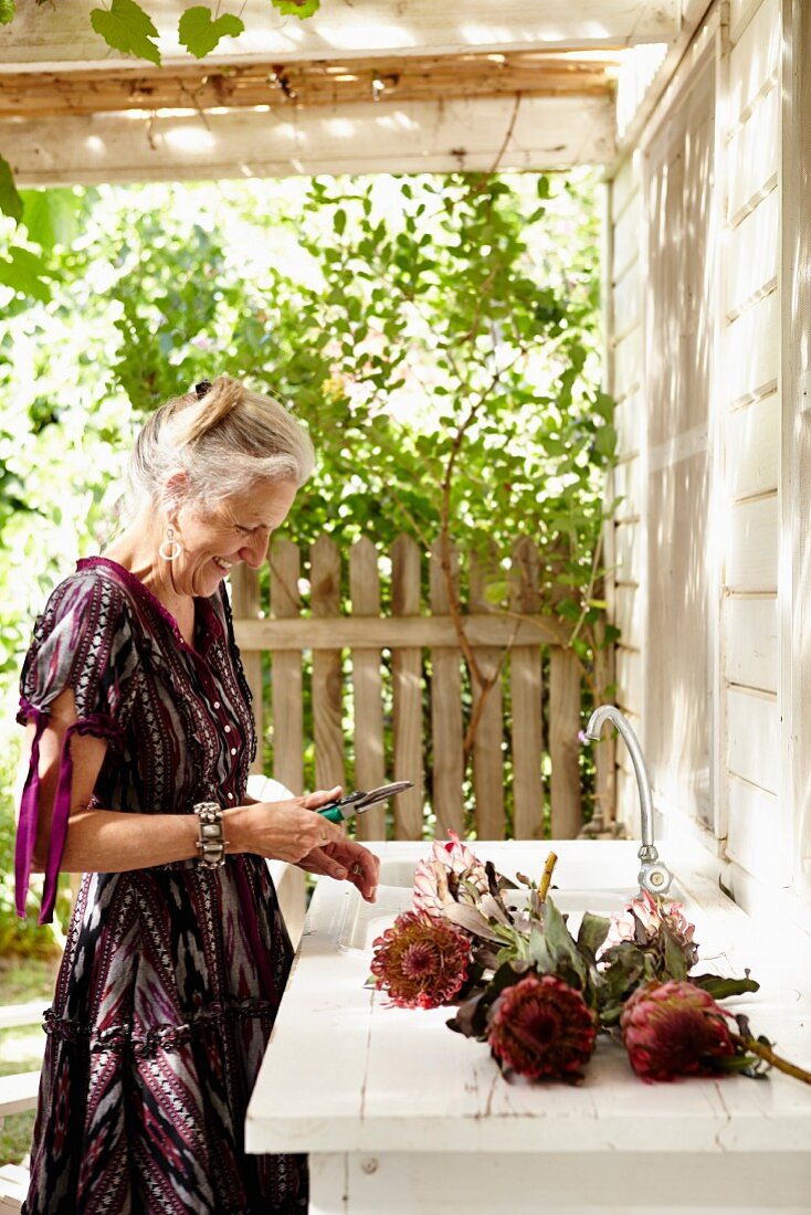 Frau mit Protea, auf Terrasse mit Spülbecken, vor Wohnhaus