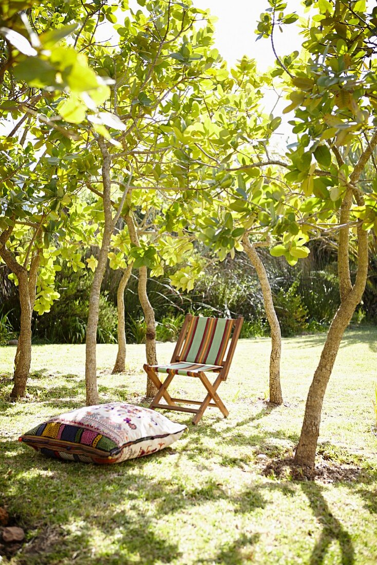 Bodenkissen und schlichter Klappstuhl aus Holz mit Streifenbezug in sommerlichem Garten