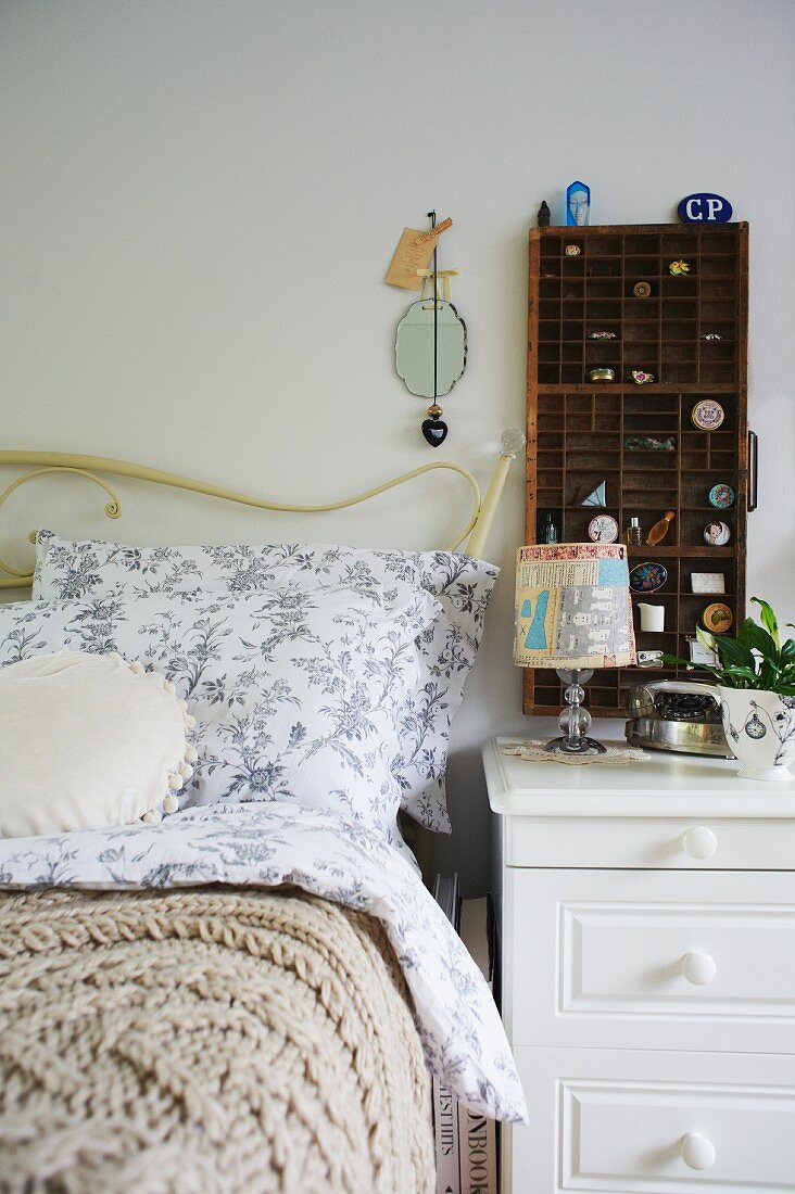 Bett mit weißem, gebogenem Gestell und romantischer Bettwäsche, daneben weisses Nachtkästchen mit Setzkasten