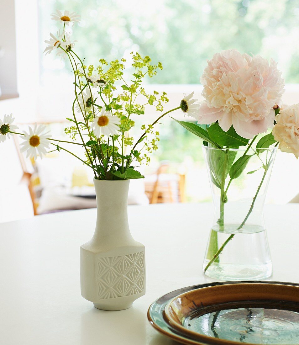 Garden flowers in white retro vase and peony in glass vase on white table