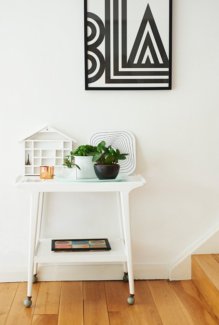 Retro side table on castors below framed geometric picture on white wall