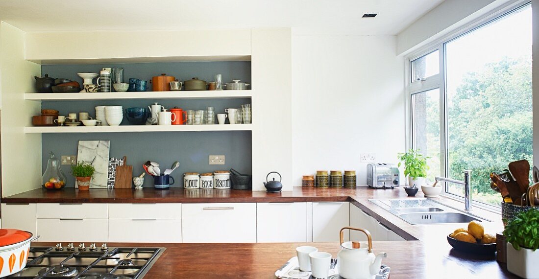 Regal mit Geschirr in grau getönter Wandnische, Küchenzeile in U-Form mit Holzarbeitsplatte