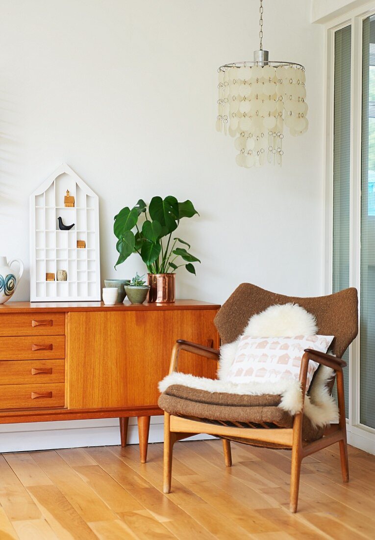 Sheepskin rug on fifties-style armchair, partially visible sideboard and ceiling lamp with lampshade made from circular pendants in corner