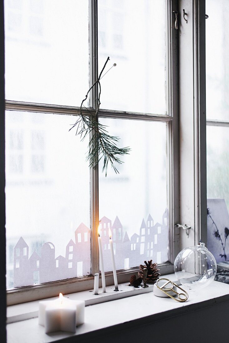 Paper city skyline stuck to window, candles and pine cones on windowsill