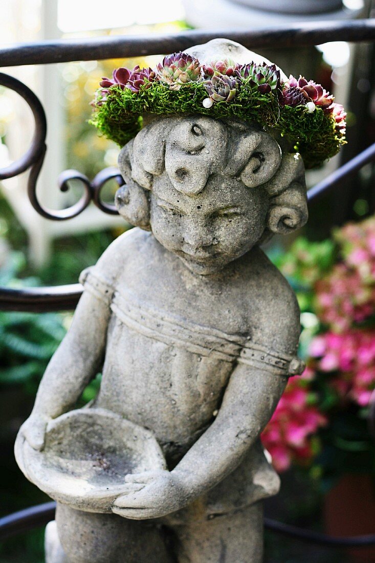Steinfigur mit Blütenkranz als Gartendekoration