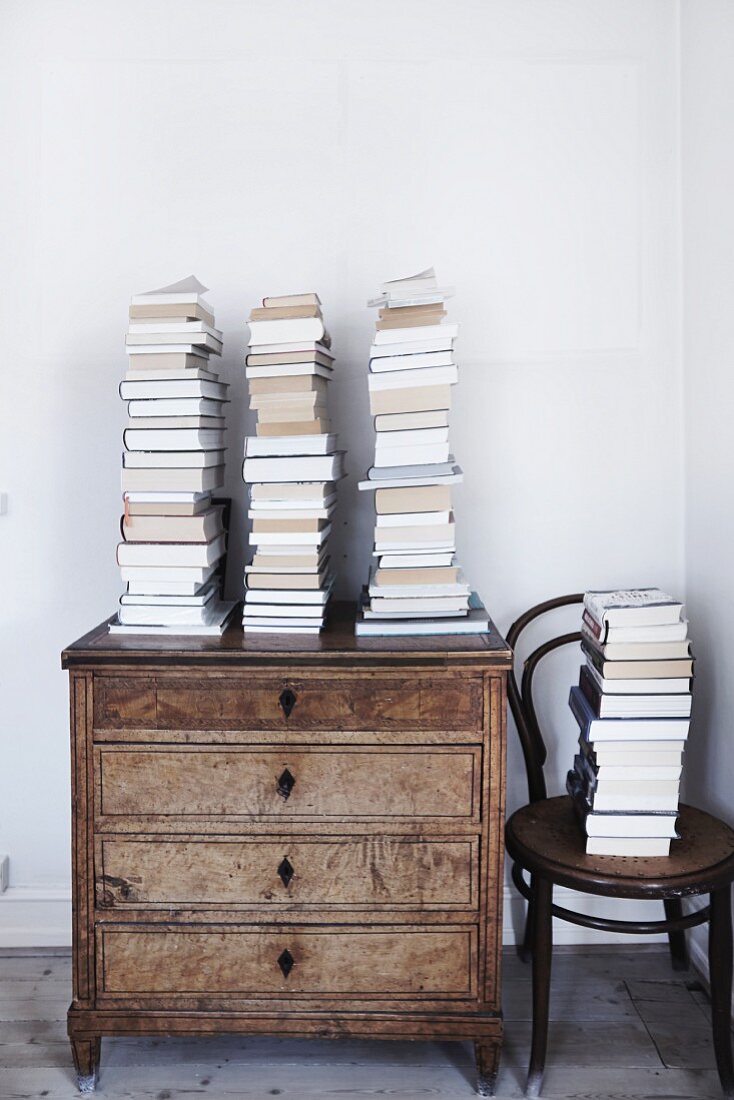 Gestapelte Bücher auf alter Kommode und daneben auf einem Thonetstuhl