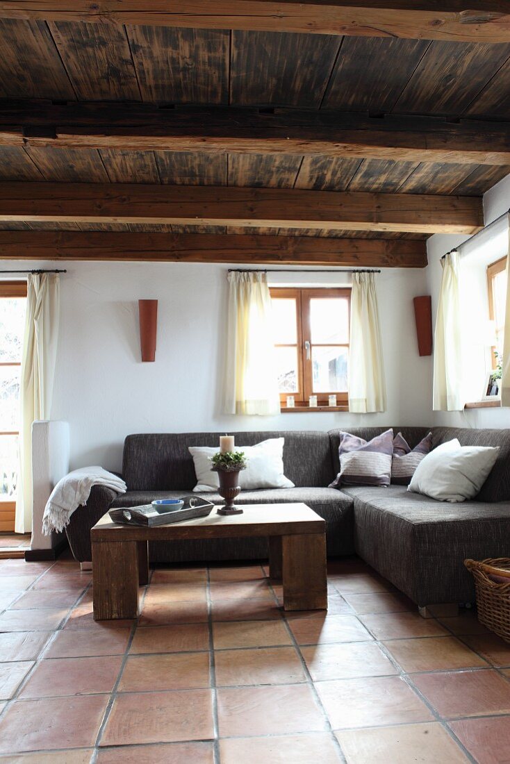 Rustic, wooden coffee table in front of comfortable corner couch in interior with wooden ceiling