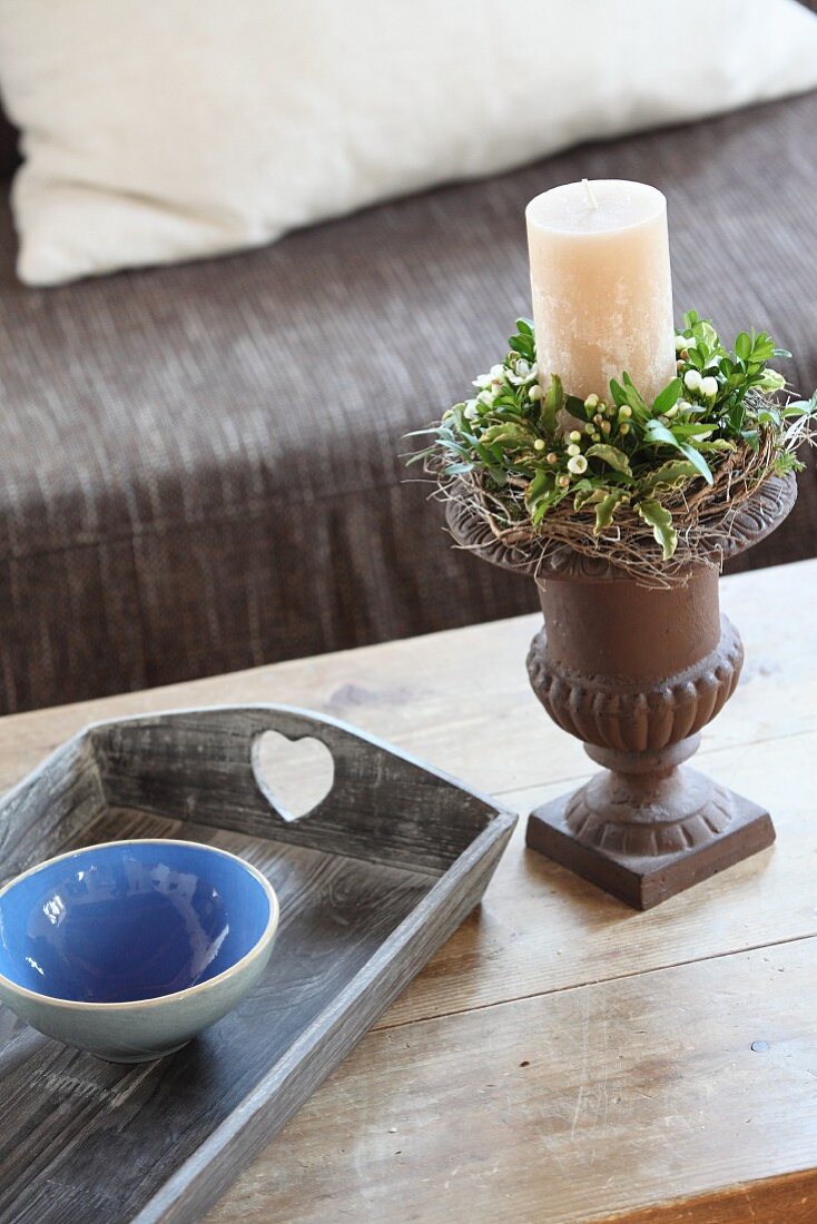 Kerzenhalter mit weisser Kerze und Blumenkränzchen neben Tablett mit blauer Keramikschale