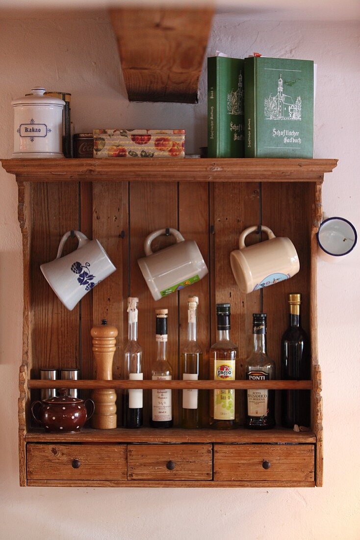 Stoneware beer mugs hanging above bottles on wooden, wall-mounted shelf unit
