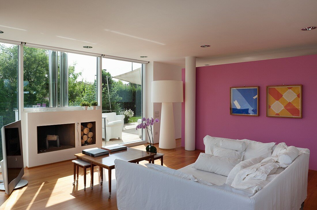 White sofa bed, set of coffee tables and open fireplace in living room with pink wall