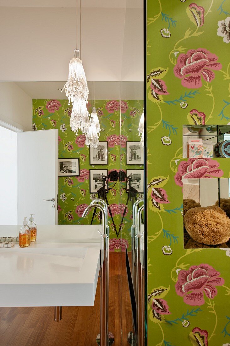Waschbecken mit Standarmatur vor vollflächigem Wandspiegel in Designerbad mit Blumentapete