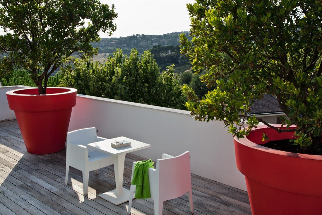 Terrasse mit modernen, weissen Kunststoff Outdoormöbeln und übergrossen Pflanzentöpfen in Rot