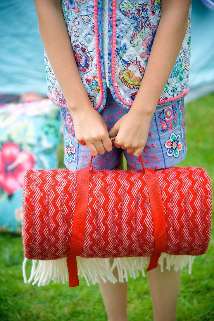 Rolled, red picnic blanket being held by girl in garden