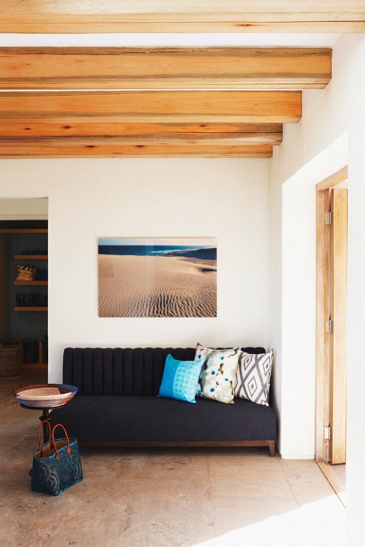 Picture of beach above sofa with scatter cushions, bowl on table and woven bag on floor