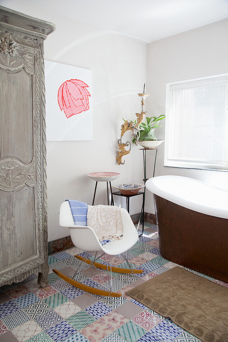 Klassiker-Schaukelstuhl neben Badewanne und antiker Schrank im Badezimmer mit bunten Bodenfliesen
