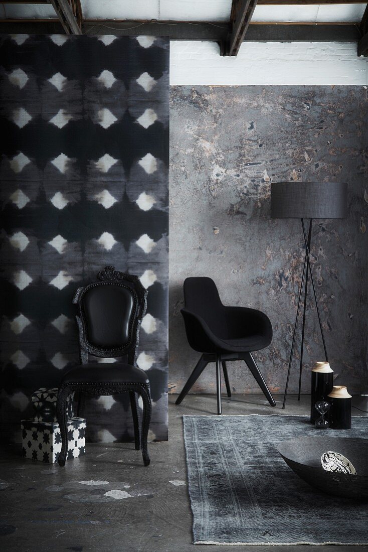 Corner furnished in shades of grey and black; black, postmodern, upholstered chair and armchair in background next to standard lamp