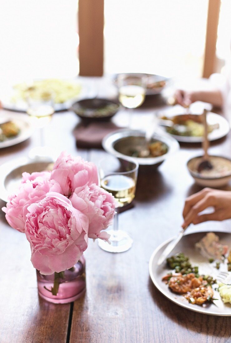 Gedeckter Tisch mit indischen Gerichten und Pfingstrosen