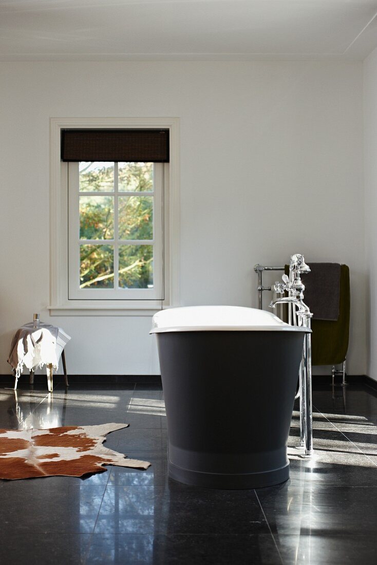 Freistehende Vintage Badewanne mit Standarmatur auf schwarzem, grossformatigem Fliesenboden, seitlich Tierfell, in minimalistischem Bad