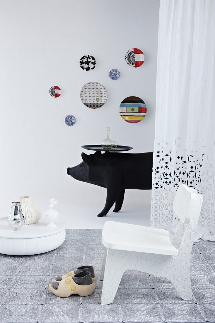 White chair and clogs on rug, black wild boar sculpture with tray table and colourful wall plates