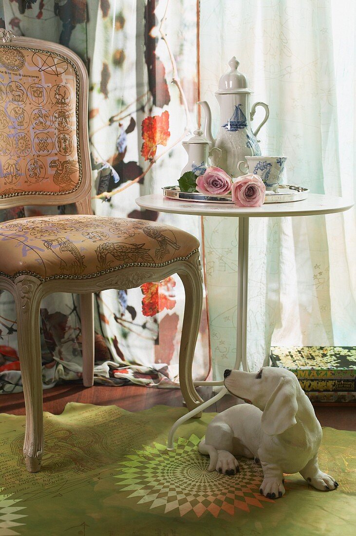 Dachshund figurine in front of Rococo chair and blue and white coffee service on modern side table