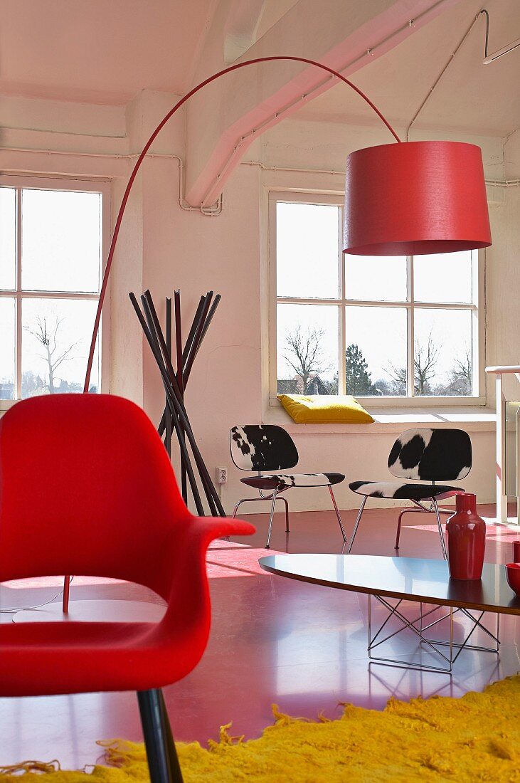 Designklassiker im Loft - roter Schalenstuhl, Bogenleuchte und Ellipsentisch, im Hintergrund Stühle mit Kuhfellbezug und ein Garderobenständer