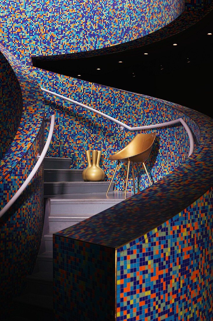 Mit bunten Mosaikfliesen belegte Brüstungsmauern an geschwungenem Treppenaufgang; gold lackierter Stuhl und Vase unter silbergrauem Handlauf
