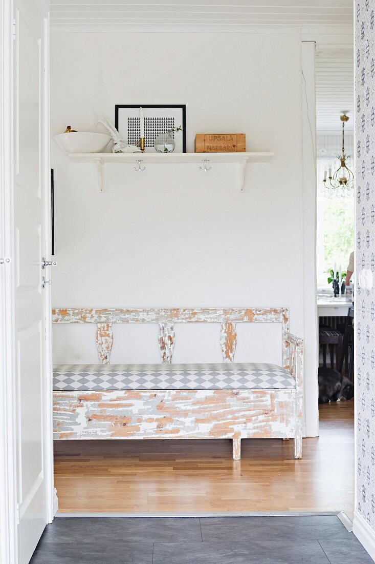 Blick durch offene Tür auf Shabby Sitzbank und weißes Regalbrett mit angelehntem Bild